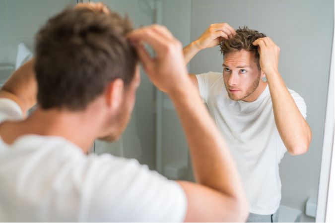 鏡をみて髪を気にしている男性